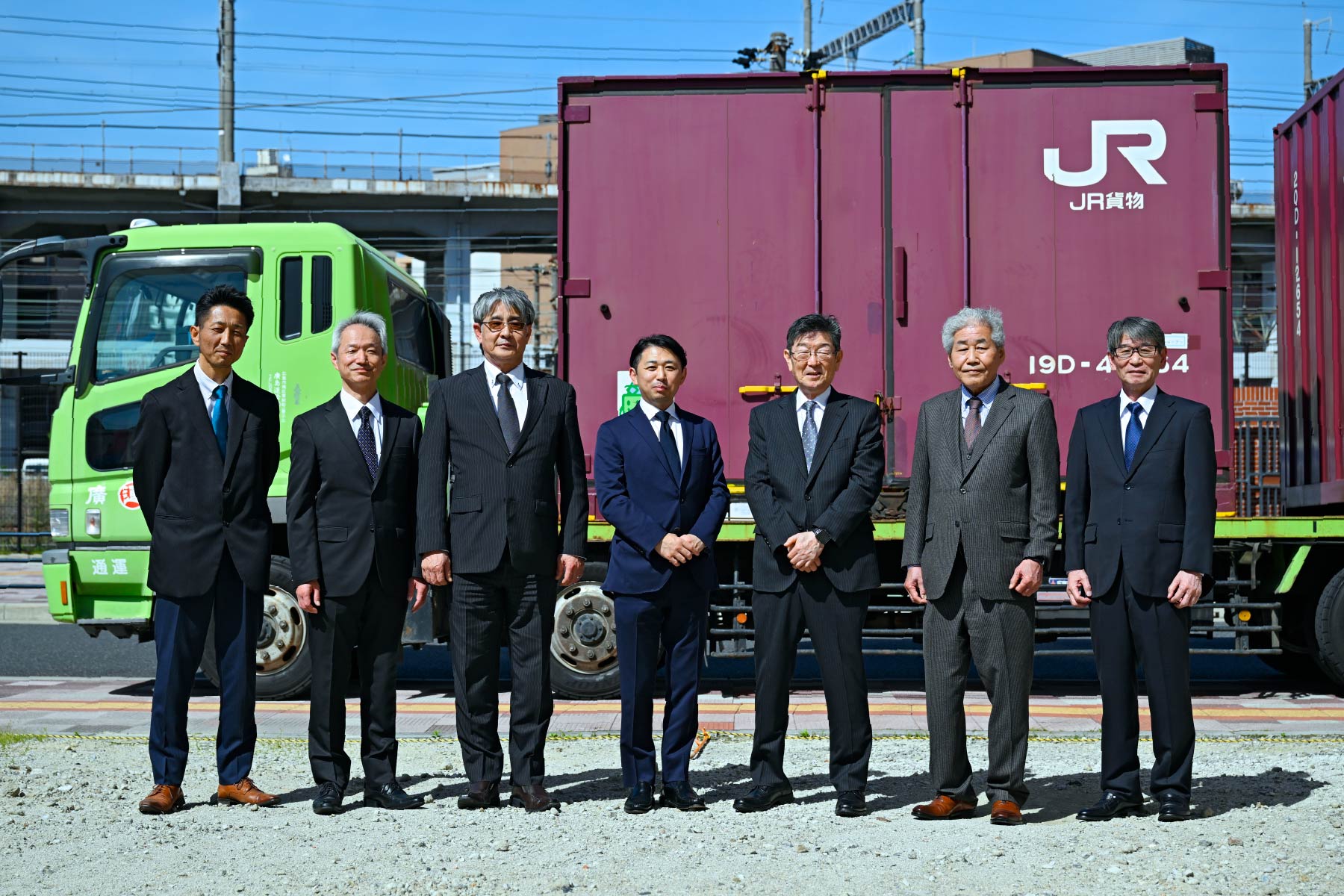 広島運輸のトラックと貨物コンテナの前に立つ社員